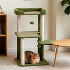 Golden cat resting beneath the tiered platforms of a green cat tree beside a wooden table.