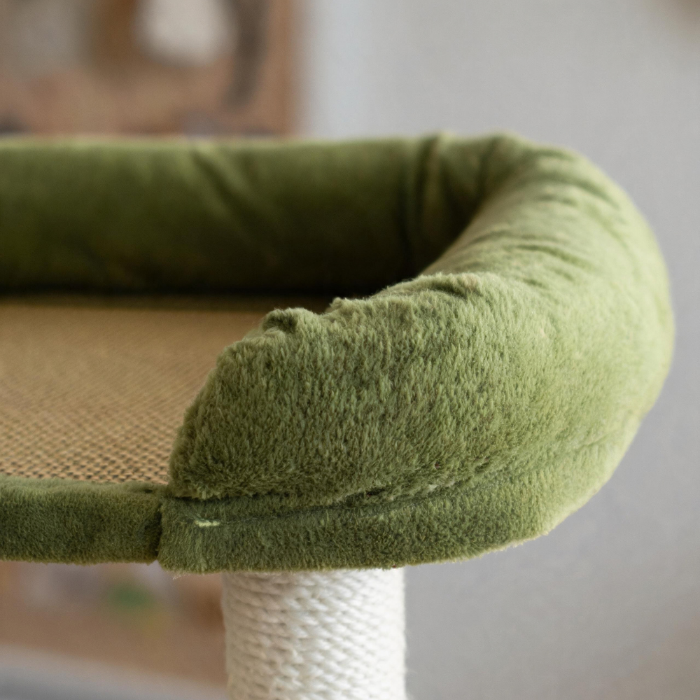Close-up of the woven rattan mat and green plush-covered edge of the cat tree’s top perch.