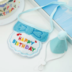 Light blue cat birthday bib with colourful Happy Birthday lettering beside a matching pom-pom party hat.