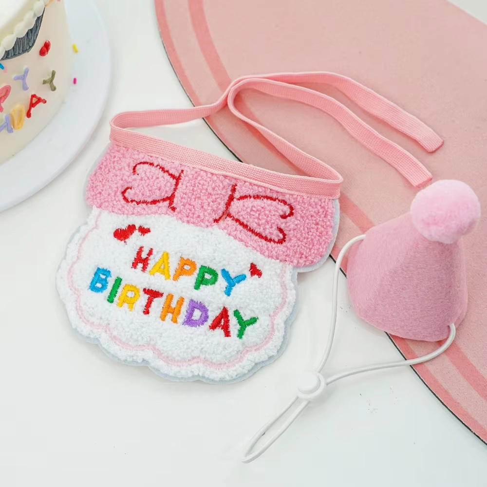 Pink cat birthday bib with a bow motif and colourful lettering beside a matching pom-pom party hat.