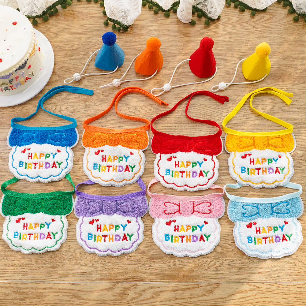 Eight colourful Happy Birthday bibs and four pom-pom party hats arranged on a wooden surface.